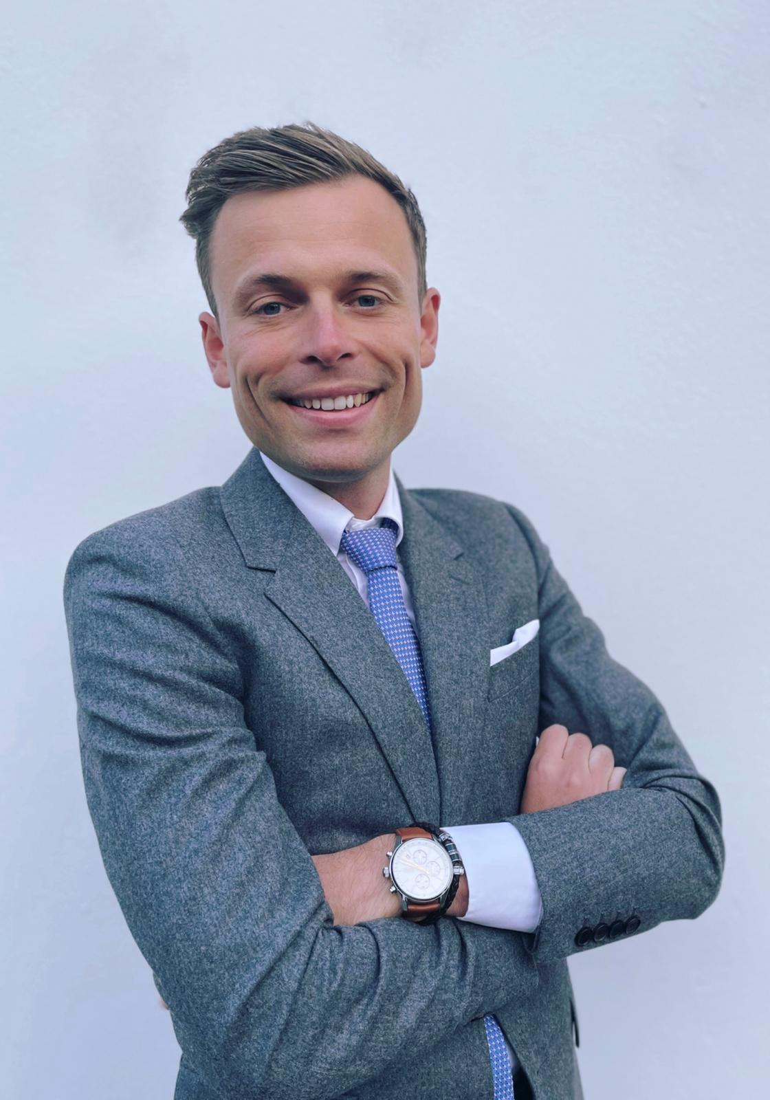 Portrait professionnel d'un avocat en costume, souriant et posant devant un fond neutre.