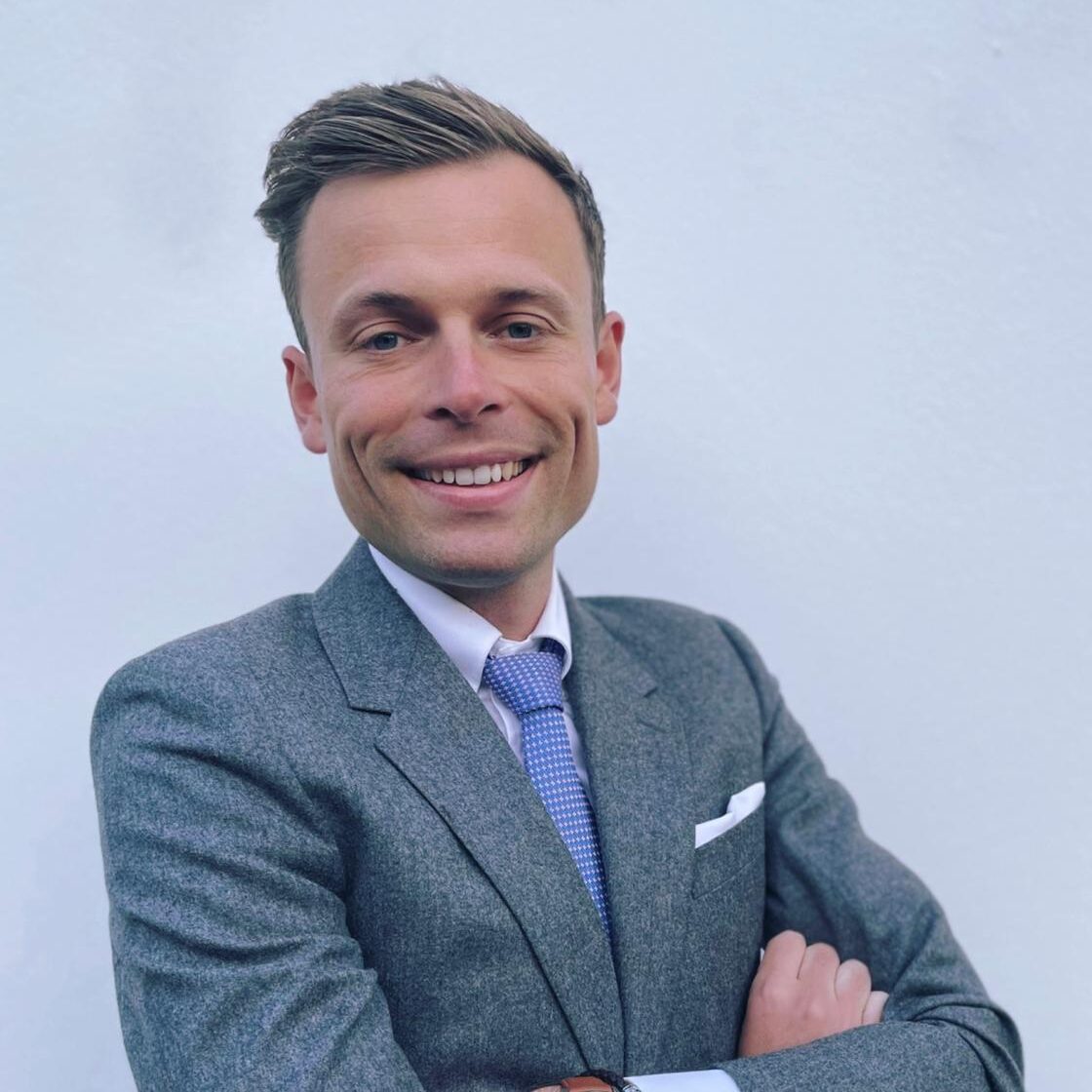 Portrait professionnel d'un avocat en costume, souriant et posant devant un fond neutre.